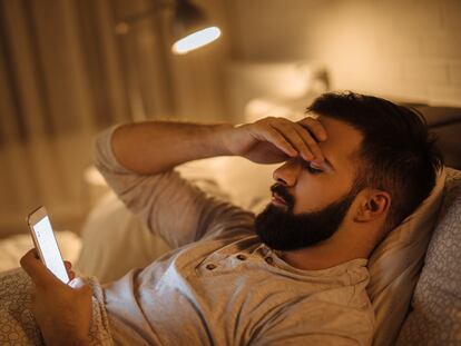 Un hombre consulta en la cama las redes sociales en su teléfono.