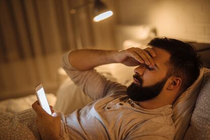 Un hombre consulta en la cama las redes sociales en su teléfono.