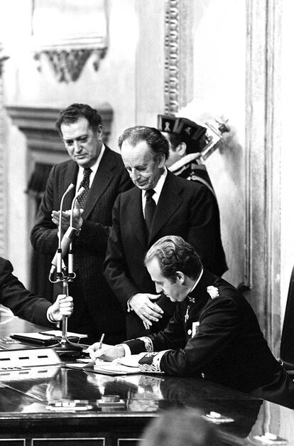 Juan Carlos I en el momento de la firma de la Constitución Española de 1978 en presencia del presidente de las Cortes, Antonio Hernández Gil, y del presidente del Congreso, Fernando Álvarez Miranda.