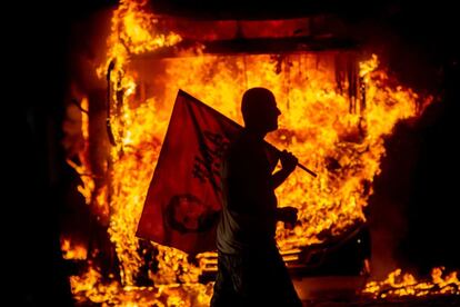 Um homem com bandeira alusiva ao ex-presidente Lula passa ao lado de ônibus em chamas no Rio de Janeiro. 