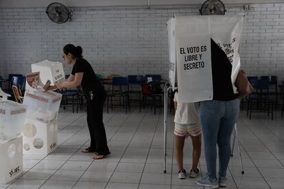 Una mujer acompañada de su hijo marca una boleta electoral dentro de una casilla, mientras otra deposita su voto en una urna, en un colegio en Saltillo. 