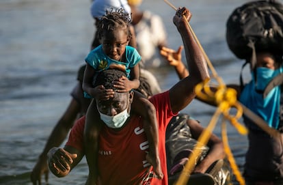 Un hombre lleva a una niña a hombros para cruzar el río Grande y recoger suministros para un campamento de migrantes, el 22 de septiembre de 2021 en Ciudad Acuña, México.