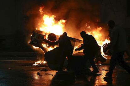 Manifestantes mueven un contenedor de basura frente a un coche de policía en llamas, en la noche del jueves en Tbilisi.

