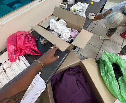 Una mujer muestra una de las cajas de ropa usada que ha heredado de una persona fallecida, en una tienda de matrículas de coches y de letreros publicitarios en la zona industrial Roodepoort, en Johanesburgo (Sudáfrica). Unos pantalones beige que Planeta Futuro ha rastreado se encuentra presuntamengte en una de estas cajas.