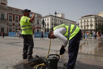 Dos trabajadores se refrescan bebiendo agua y con una manguera en el centro de Madrid, este miércoles.