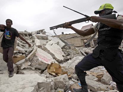 Un policía apunta a un haitiano con varios objetos cargados a su espalda.