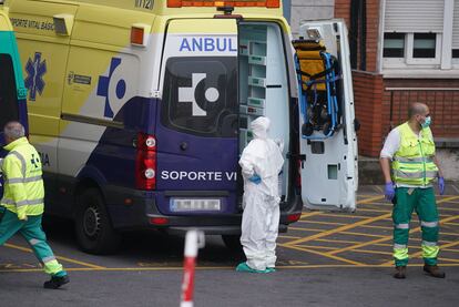 Varios sanitarios protegidos, uno con un traje y otro con mascarilla y guantes de látex, junto a una ambulancia en el Hospital Universitario Cruces de Bilbao