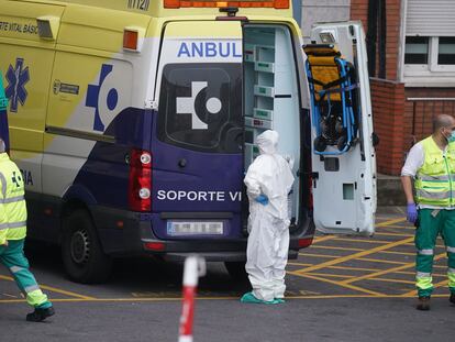 Varios sanitarios protegidos, uno con un traje y otro con mascarilla y guantes de látex, junto a una ambulancia en el Hospital Universitario Cruce en Bilbao