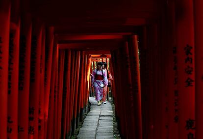 Dos mujeres vestidas con un yukata, o kimono de verano, caminan a través de varios arcos torii de madera rojos en el santuario Nezu de Tokio (Japón).