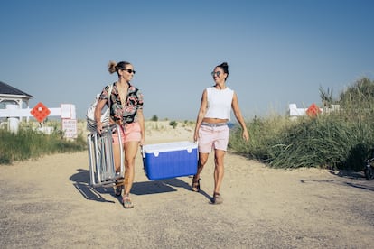 Two women carry a cooler to the beach