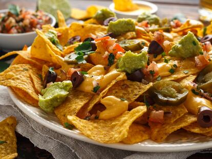 Un plato de nachos con guacamole, queso, aceitunas y chiles jalapeños.