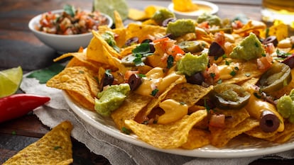 A plate of nachos with guacamole, cheese, olives and jalapeño peppers.