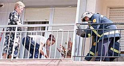 Un bombero y una vecina recogen cristales rotos, ayer, tras la explosión de la carcasa en la Malva-rosa.