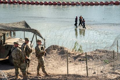 Asylum-seeking migrants walk in the Rio Grande river between a floating fence and the river bank as they look for an opening in a concertina wire fence to land on U.S. soil in Eagle Pass, Texas