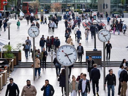 Trabajadores caminando bajo los relojes de Nash Court en el corazón del distrito financiero de Canary Wharf en Londres.