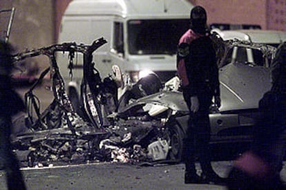 Un agente de la Ertzaintza, ante los restos del coche destrozado tras la explosión en Bilbao. PLANO GENERAL