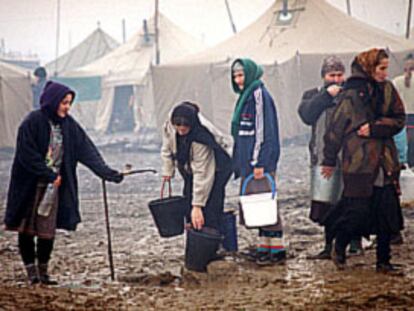 Mujeres chechenas toman agua potable de un surtidor en un campo de refugiados.