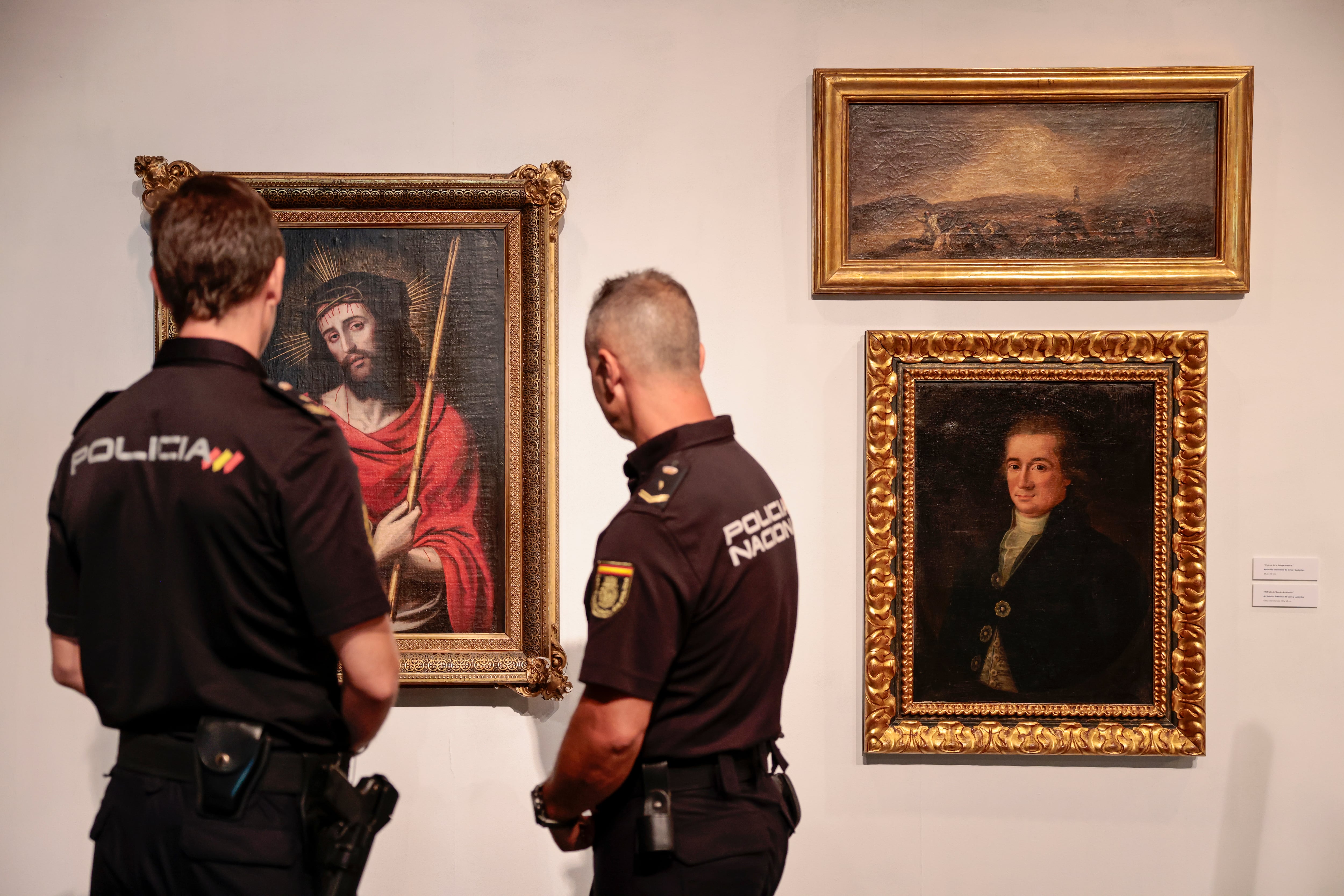 Dos agentes de la Policía Nacional contemplan tres obras de arte falsas incautadas en una operación en Valencia, en 2023.