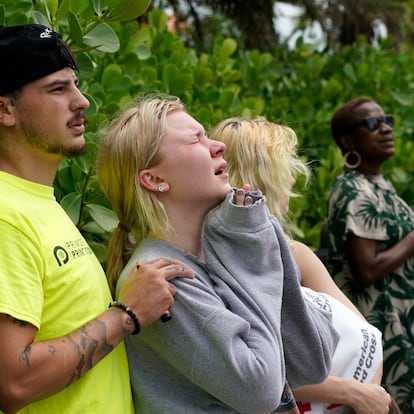 Ariana Hevia, of New Orelans, La., center, stands with Sean Wilt, left, near the 12-story beachfront condo building which partially collapsed, Friday, June 25, 2021, in the Surfside area of Miami. Hevia' s mother Cassandra Statton lives in the building. Search and rescue teams continue to work at the site hoping to detect any sounds coming from survivors. (AP Photo/Lynne Sladky)