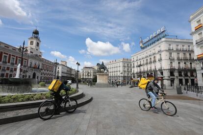 Dos repartidores de la empresa Glovo en la Puerta del Sol el día en que el sindicato UGT ha enviado un requerimiento a Glovo, Deliveroo y UberEats para que no aprovechen el estado de alarma para modificar las condiciones de trabajo, ha denunciado que "muchos" trabajadores emplean 70 horas a la semana y ha advertido de que podría convocar una huelga en sector, este lunes en Madrid.