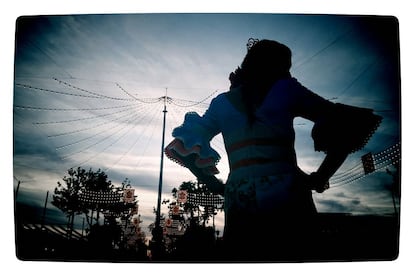 La silueta de una mujer vestida de flamenca se dibuja en el cielo con el alumbrado ya encendido.