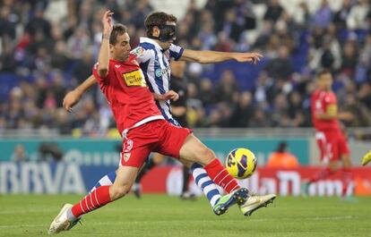 Stuani, con máscara protectora, pelea un balón con Fernando Navarro.