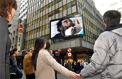 Un grupo de viandantes en el centro de Hong Kong prestan atención a una pantalla que informa sobre la captura de Sadam Husein.