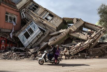 Una pareja en moto pasa por delante de edificios derruidos por los terremotos, este domingo en Adiyaman.