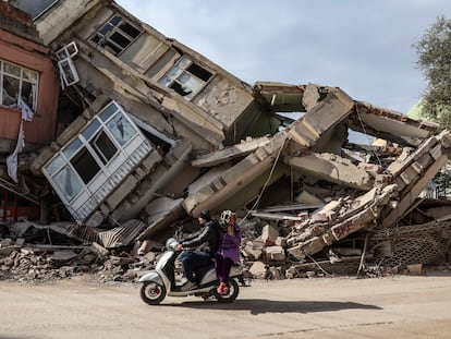 Una pareja en moto pasa por delante de edificios derruidos por los terremotos, este domingo en Adiyaman.