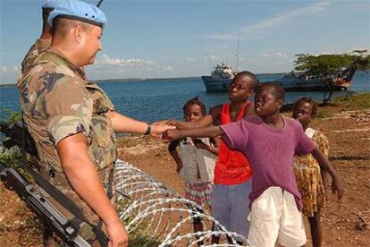 Soldados españoles saludan, por encima de una alambrada, a niños haitianos.