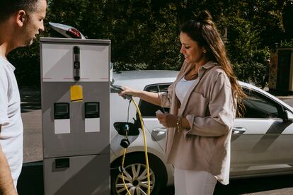 Madre sonriente sosteniendo un enchufe eléctrico parada junto al padre en una gasolinera.