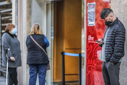 Un hombre joven mira su móvil mientras espera a la puerta de una oficina de empleo en Valencia.