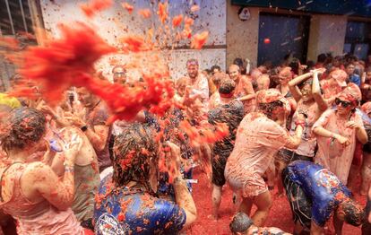 Varios grupos de asistentes a la fiesta de la Tomatina se lanzan tomates unos a otros.