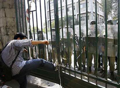 Un estudiante trata de abrir a patadas una puerta del campus de la Universidad de Tehern frente a un grupo de policas.