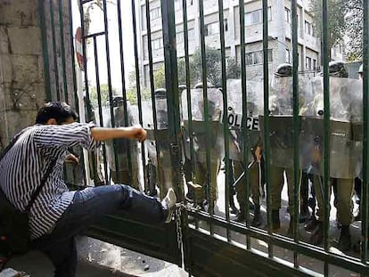 Un estudiante trata de abrir a patadas una puerta del campus de la Universidad de Teherán frente a un grupo de policías.