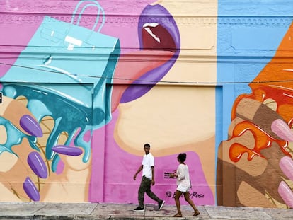 Una pareja atraviesa una pared adornada con un grafiti en el barrio de Wynwood, Miami.