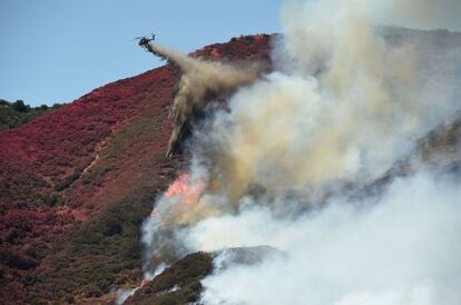 TOPSHOT - A helicopter drops fire water on a burning hillside in Keenbrook, California on August 18, 2016. 
The Blue Cut Fire has charred more than 35,000 acres causing more than 80,000 people to be evacuated from their homes. / AFP PHOTO / Josh Edelson