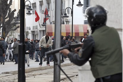 Los manifestantes lanzan piedras a un policía mientras les apunta con un arma de fuego.