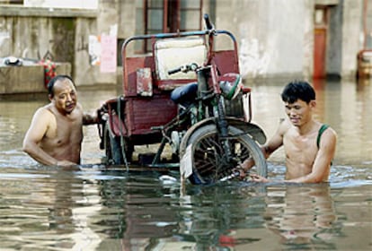 Dos habitantes de Yueyang tratan de salvar un triciclo motorizado de la riada.