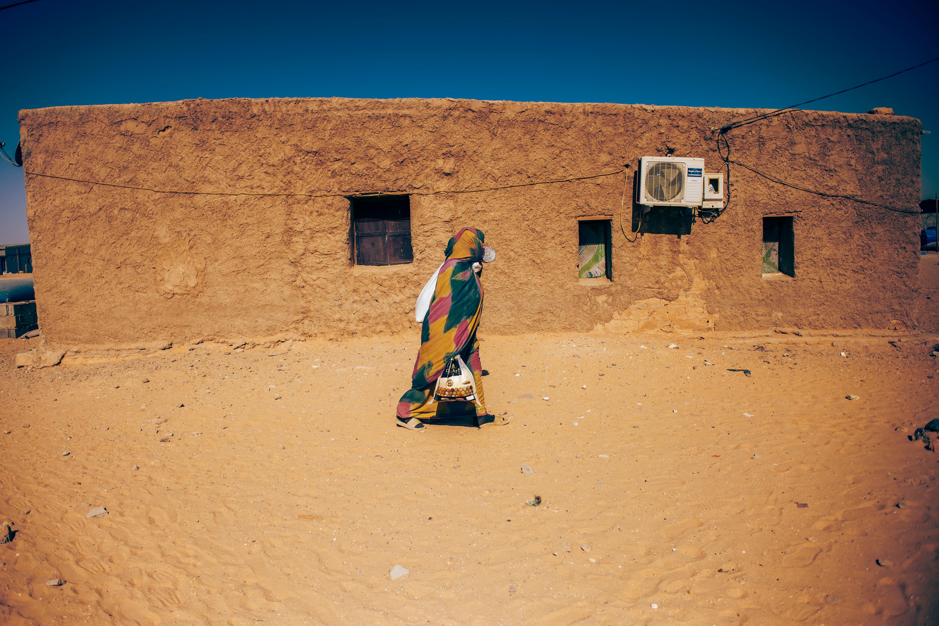 Una mujer saharaui pasa ante una casa de adobe en el campamento de refugiados de Auserd, en la región de Tinduf, Argelia, el 5 de mayo de 2024. 