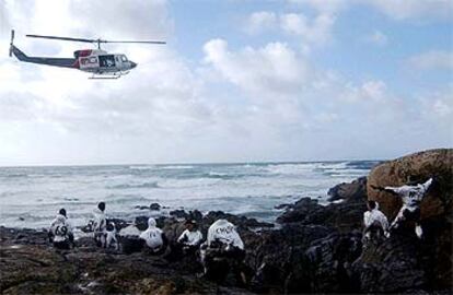 Un helicóptero sobrevuela a un grupo de soldados que limpia chapapote cerca de Carnota.