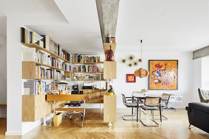 Una estantería de roble y acero lacado es a la vez mueble y habitación. La ideó el arquitecto que reformó el piso, Gustau Gili Galfetti (GGG), inspirándose en la obra del francés Jean Prouvé. El escritorio lo diseñó George Nelson en 1958. De ese mismo año es la silla de oficina modelo Aluminium de los Eames, que produce la empresa Vitra. La lámpara que cuelga sobre la mesa del comedor es el modelo Disa, de José Antonio Coderch. Marcel Breuer, autor del Met Breuer de Nueva York (antiguo Museo Whitney), diseñó en 1928 las sillas Cesca —en el comedor— y las bautizó con el nombre de su hija. En la pared, a la derecha, un mosaico cerámico de Armand Oliver Milián reinterpreta un dibujo de Cliff Roberts, y la escultura mural de latón con forma de erizo es de Curtis Jeré