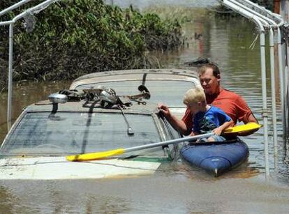 Un padre y su hijo en una canoa junto a vehículos anegados en la ciudad de Bundaberg.