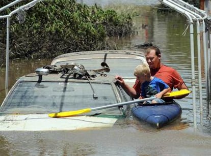 Un padre y su hijo en una canoa junto a vehículos anegados en la ciudad de Bundaberg.