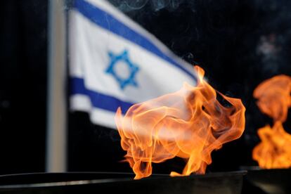 Una antorcha prende durante la celebración del Día del Recuerdo del Holocausto con una bandera de Israel en segundo plano.