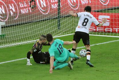 El delantero bosnio del Real Madrid, Luka Jovic, en el suelo, disputa un balón en el área junto a Carlos Soler, centrocampista español del Valencia CF, y el portero, Jaume Doménech.