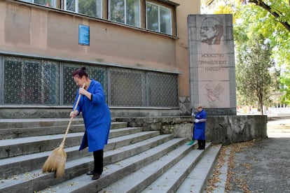 Dos limpiadoras barren las escaleras de un edificio que luce un monumento con la imagen de Lenin en Simferopol, Crimea.