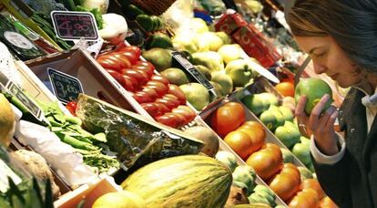 Una mujer huele una manzana en un puesto de frutas en un mercado de Madrid.