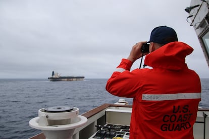 A US Coast Guard official looking through binoculars as the ship Marinera (previously named Bella 1) is seen in the distance at sea.