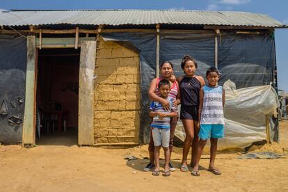 <p>Estela Sierra, 30 años, posa con sus hijos delante de la casa que comparten en Villa del Sur, en Riohacha (La Guajira). Viven en un asentamiento informal entre colombianos, venezolanos y retornados. La constante amenaza de desalojo pesa como una losa encima de ellos. Ante la falta de trabajo, Sierra se vio obligada a ocupar el terreno junto con otras familias que tampoco tenían dónde vivir. "Esto era puro monte", dice señalando su alrededor bajo un sol que abrasa. "Había árboles muy grandes, culebras, insectos... incluso un día encontramos el cadáver de un hombre. Me daba miedo, pero no había alternativa. No conocía a nadie. Era horrible, sin luz, sin agua".</p> <p>Su vivienda está construida con materiales precarios. El techo está a medias, porque no había dinero para más. "¿Cómo consigo el dinero? No quisiera ni acordarme", lamenta. "Vivimos con la incertidumbre del desalojo. Si eso pasa, ¿adónde vamos?".</p>